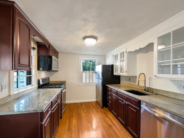 kitchen featuring a textured ceiling, appliances with stainless steel finishes, sink, light stone counters, and light wood-type flooring