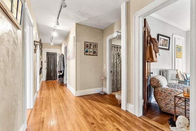 corridor with track lighting, light wood-style floors, baseboards, and crown molding