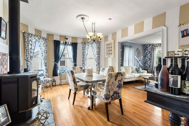 dining space featuring wallpapered walls, a chandelier, a wood stove, plenty of natural light, and light wood-style floors