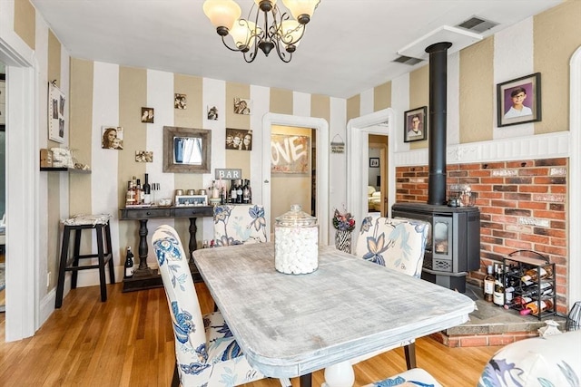 dining space with wallpapered walls, a wood stove, wood finished floors, and a chandelier