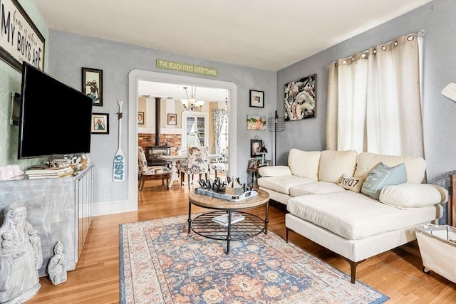 living room featuring a chandelier, light wood-style floors, a wood stove, and baseboards