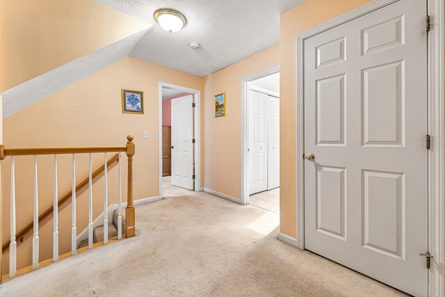 hallway featuring light carpet, lofted ceiling, and a textured ceiling