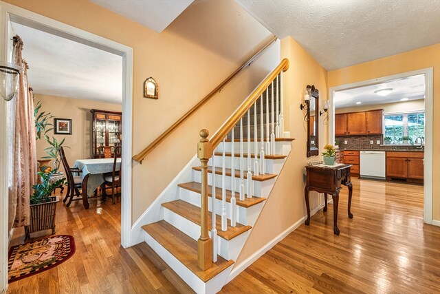 staircase with a textured ceiling, sink, and hardwood / wood-style floors