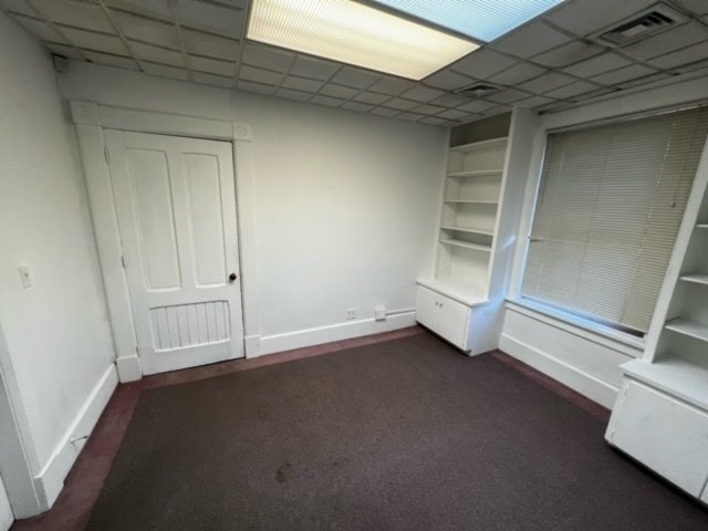 unfurnished bedroom with a paneled ceiling and dark carpet