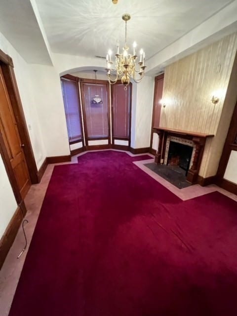 unfurnished living room featuring light carpet, a brick fireplace, and a notable chandelier