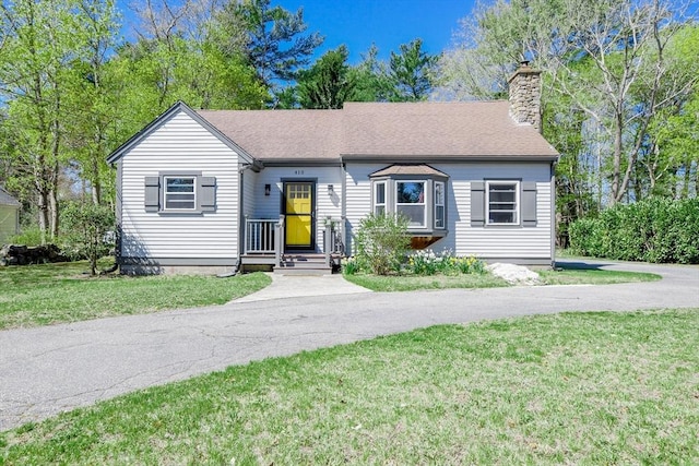 view of front of house featuring roof with shingles, a chimney, and a front yard