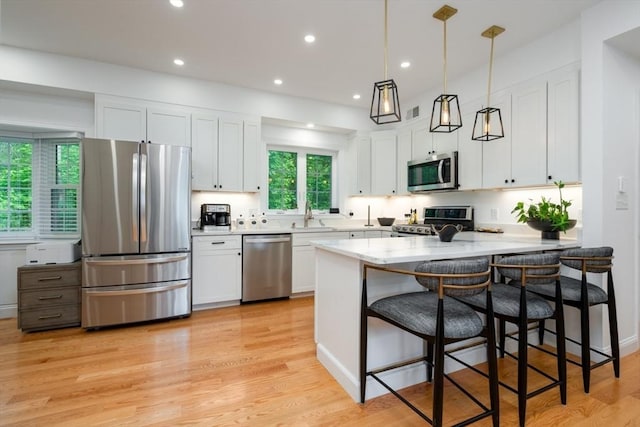 16 Border Rd, Reading, MA 01867 - kitchen featuring stainless steel appliances, a peninsula, white cabinets, a kitchen bar, and light wood-type flooring