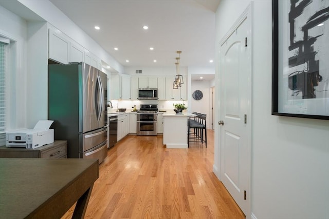 16 Border Rd, Reading, MA 01867 - kitchen with appliances with stainless steel finishes, a breakfast bar, white cabinetry, light wood-type flooring, and recessed lighting