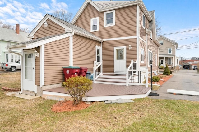 rear view of property featuring a lawn and fence