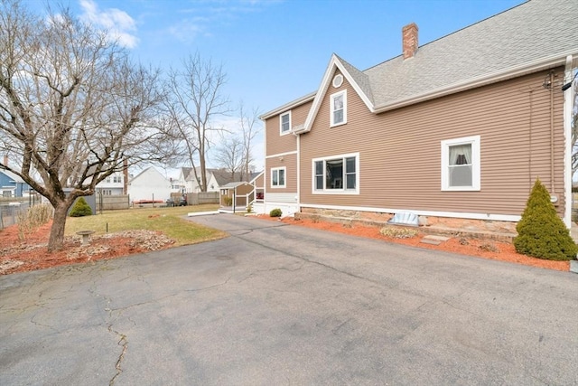 view of home's exterior featuring roof with shingles, a yard, a chimney, and fence