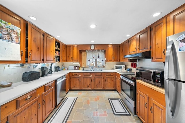 kitchen featuring under cabinet range hood, light countertops, appliances with stainless steel finishes, brown cabinets, and stone tile flooring