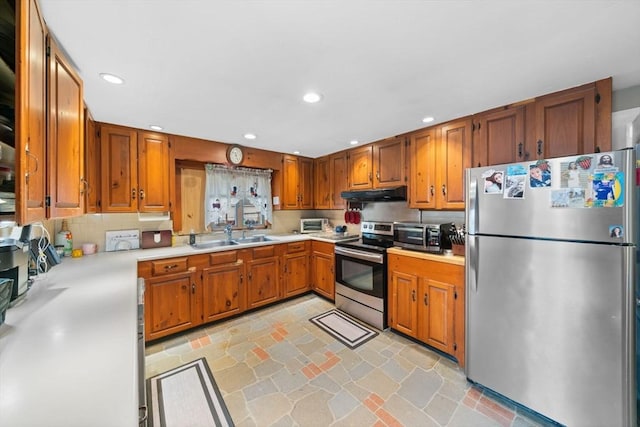 kitchen with light countertops, appliances with stainless steel finishes, brown cabinetry, and under cabinet range hood