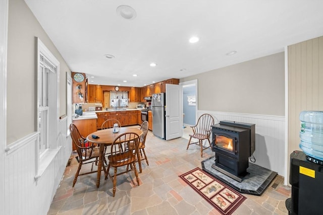 dining space with a wainscoted wall, stone finish floor, a wood stove, and recessed lighting