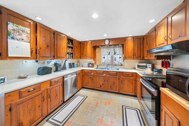 kitchen featuring brown cabinets, stone tile floors, stainless steel appliances, a sink, and under cabinet range hood