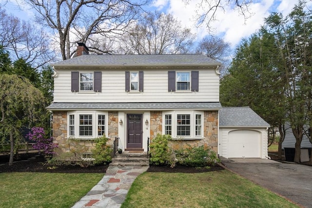 colonial house featuring an attached garage, roof with shingles, driveway, and stone siding