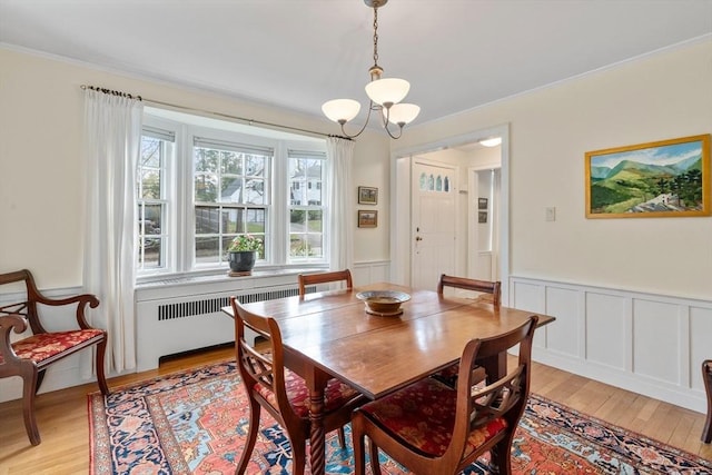 dining area featuring crown molding, wainscoting, light wood finished floors, a chandelier, and radiator