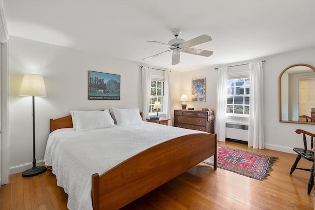 bedroom with wood-type flooring, radiator, baseboards, and multiple windows