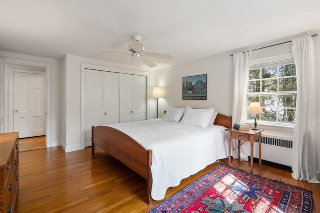 bedroom featuring a ceiling fan, wood finished floors, baseboards, a closet, and radiator heating unit