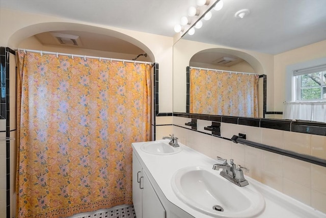 full bath featuring visible vents, a sink, double vanity, and tasteful backsplash