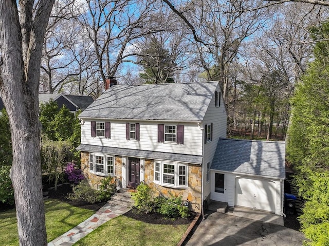 colonial home with roof with shingles, a front lawn, stone siding, a garage, and a chimney
