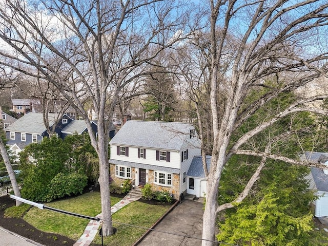 traditional home with a garage, a front lawn, stone siding, roof with shingles, and driveway