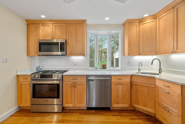 kitchen with decorative backsplash, light countertops, a sink, light wood finished floors, and stainless steel appliances