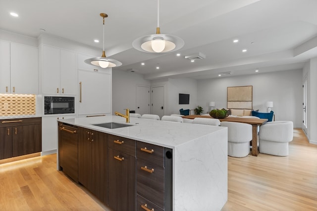 kitchen with sink, white cabinetry, pendant lighting, light hardwood / wood-style flooring, and a center island with sink