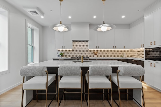 kitchen with oven, tasteful backsplash, a kitchen breakfast bar, a kitchen island with sink, and decorative light fixtures