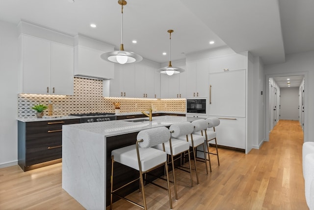 kitchen featuring white cabinets, light hardwood / wood-style floors, decorative light fixtures, and a kitchen island with sink