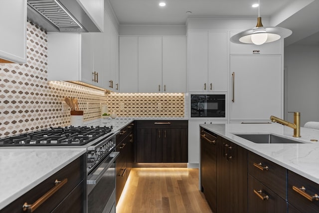 kitchen featuring wall chimney range hood, high end stainless steel range, sink, decorative light fixtures, and white cabinets