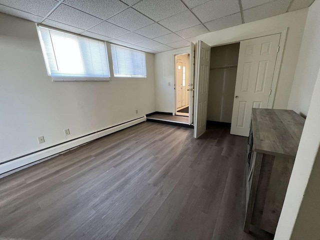 unfurnished bedroom with dark hardwood / wood-style flooring, baseboard heating, a drop ceiling, and a closet