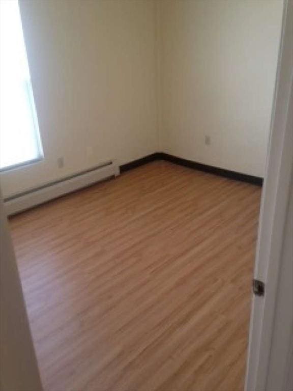 unfurnished room with a baseboard heating unit and light hardwood / wood-style flooring