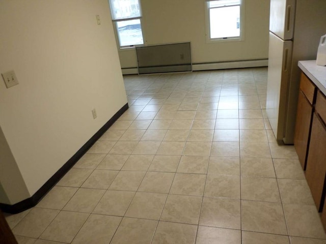 empty room featuring baseboard heating, a wealth of natural light, and light tile patterned flooring