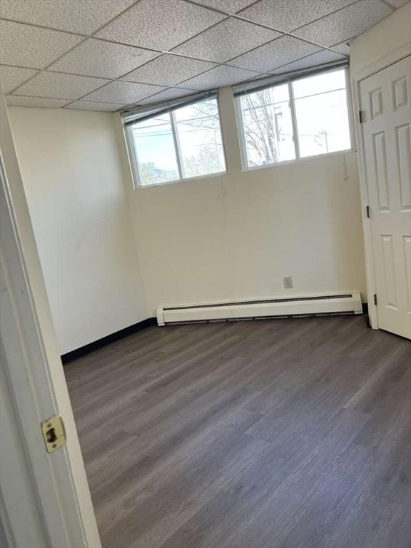 empty room with a drop ceiling, dark hardwood / wood-style flooring, and a baseboard heating unit