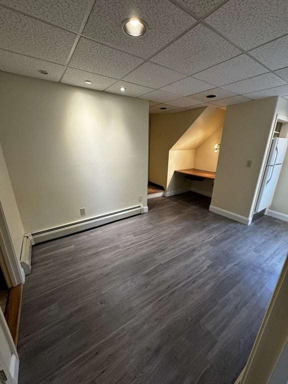 basement with a drop ceiling, dark hardwood / wood-style floors, and a baseboard heating unit