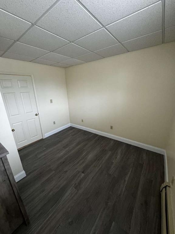 spare room with baseboard heating, a drop ceiling, and dark wood-type flooring