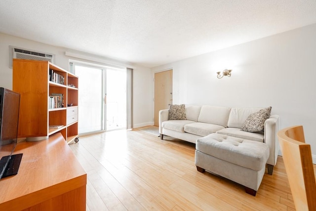 living room with light wood-type flooring, a wall mounted air conditioner, and a textured ceiling