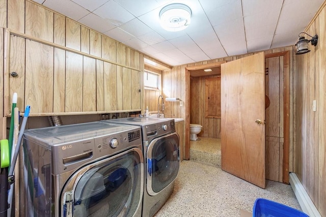 washroom with washing machine and dryer, sink, a baseboard radiator, and wood walls