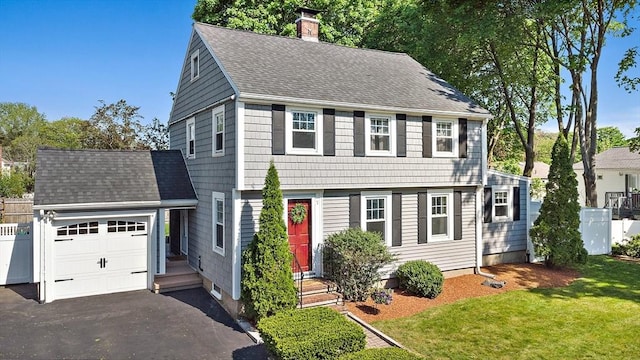 colonial inspired home with a chimney, roof with shingles, and asphalt driveway