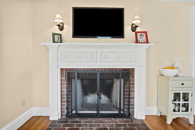 detailed view of a brick fireplace, baseboards, and wood finished floors