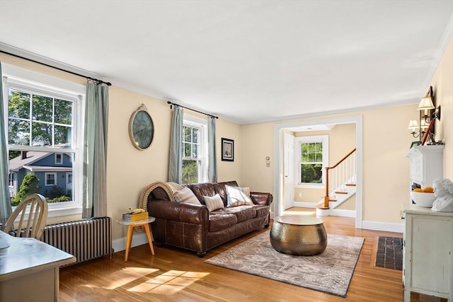 living area with light wood-type flooring, baseboards, radiator heating unit, and stairs