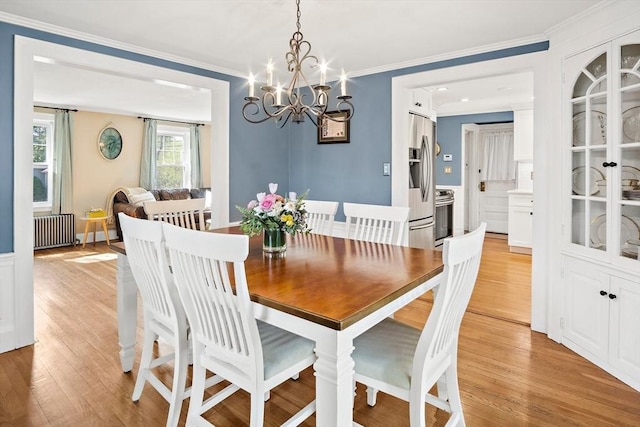 dining area with radiator heating unit, a chandelier, light wood-style floors, and crown molding