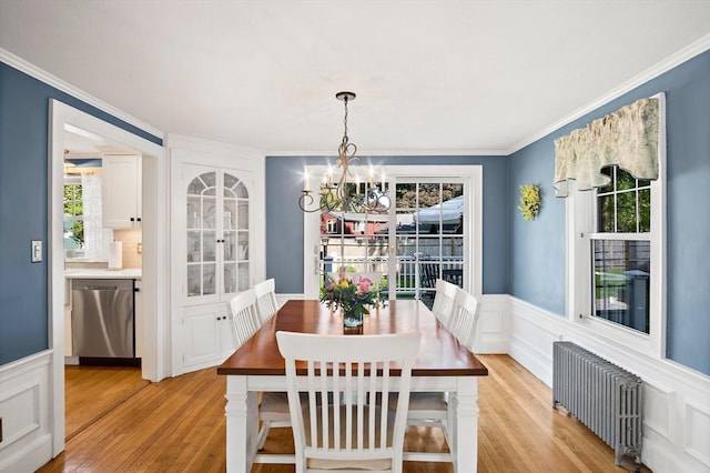 dining area featuring radiator heating unit, a chandelier, plenty of natural light, light wood finished floors, and wainscoting