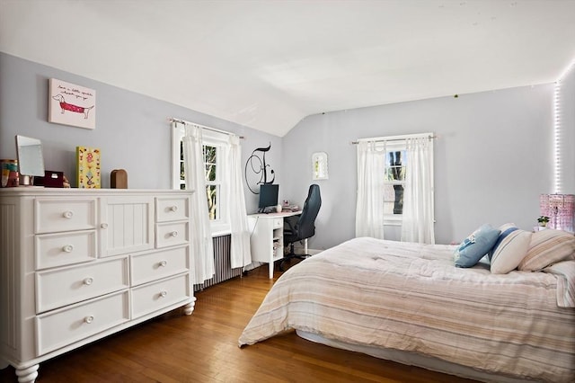 bedroom featuring vaulted ceiling, multiple windows, dark wood-style flooring, a desk, and radiator