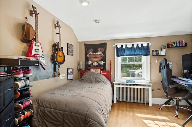 bedroom featuring radiator, wood finished floors, an office area, vaulted ceiling, and baseboards