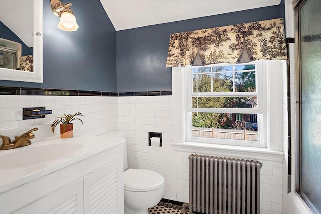 bathroom featuring radiator heating unit, tile walls, toilet, vanity, and an enclosed shower