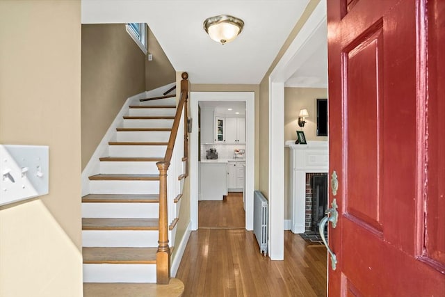 entryway with stairway, wood finished floors, and a brick fireplace