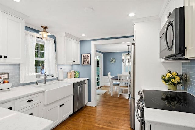 kitchen featuring appliances with stainless steel finishes, a sink, backsplash, light wood finished floors, and white cabinetry