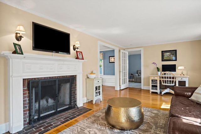 living area with wood finished floors, a brick fireplace, ornamental molding, a desk, and french doors