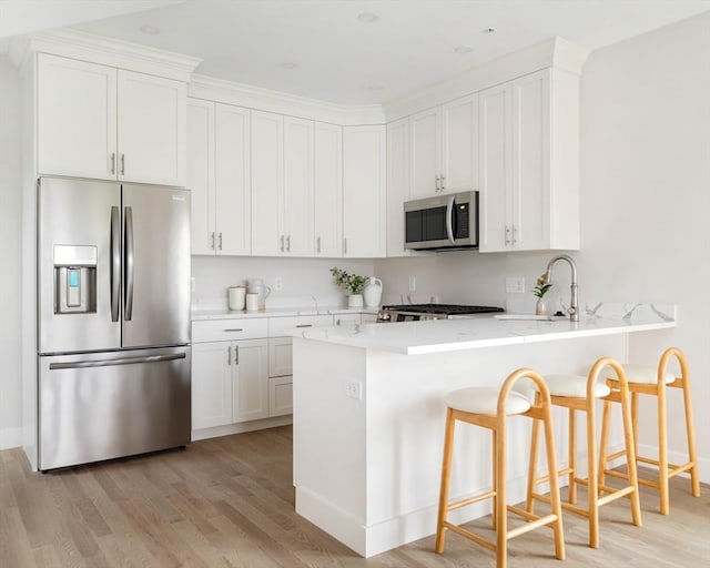 kitchen featuring stainless steel appliances, a sink, light wood-type flooring, light countertops, and a peninsula